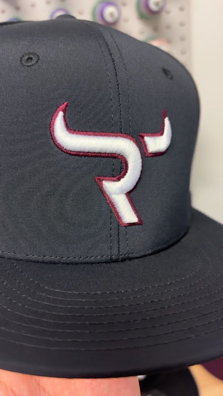 Close-up of a white 3D puff logo with maroon outline on a black cap