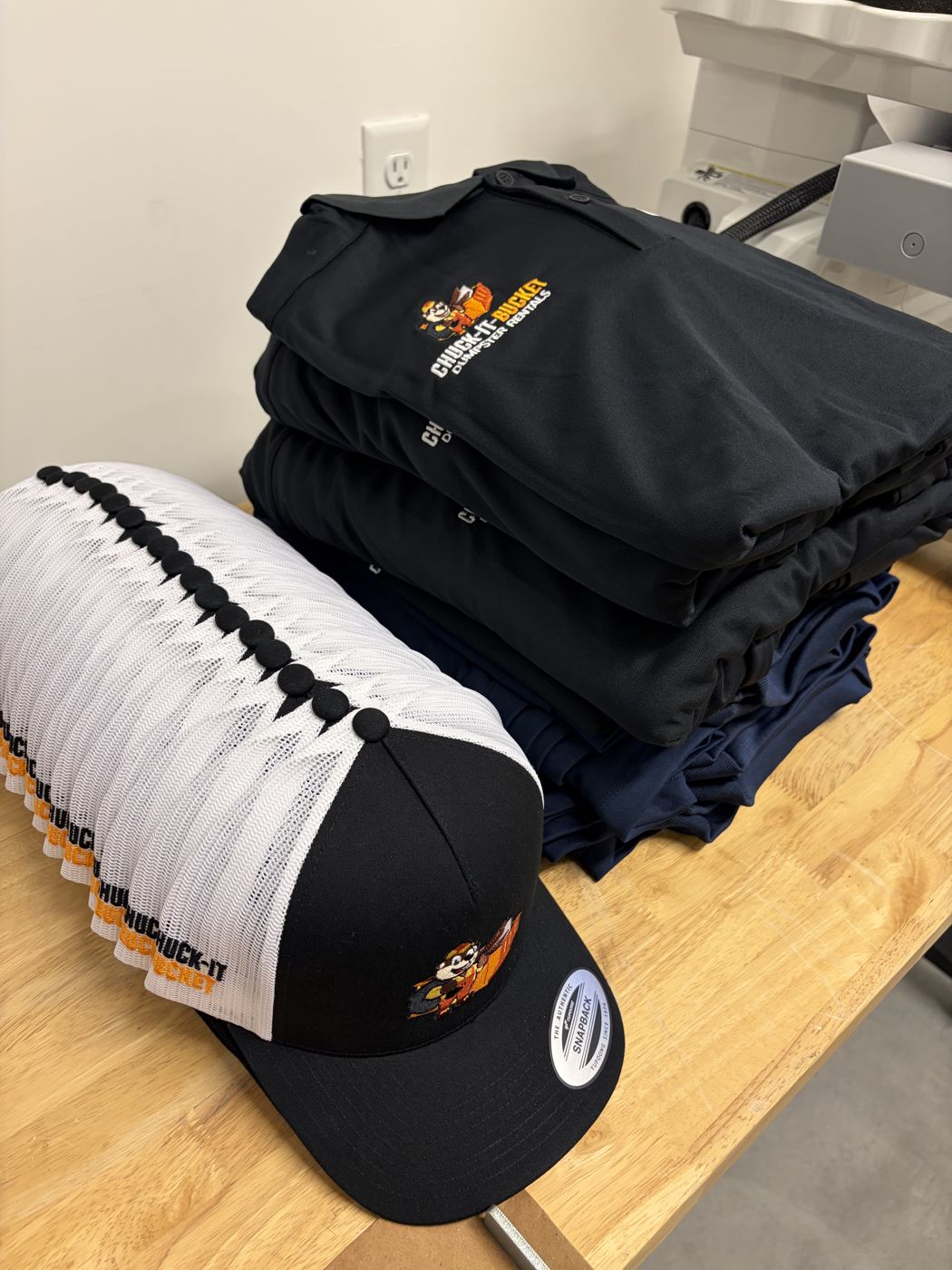 Stack of embroidered company polos and trucker hats