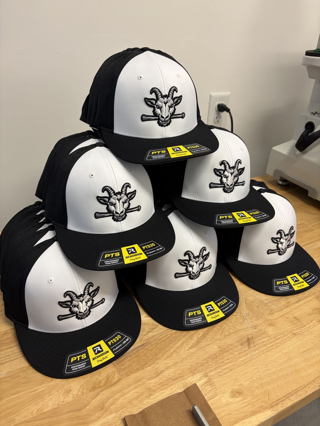 Stack of black and white performance caps with a 3D goat mascot logo